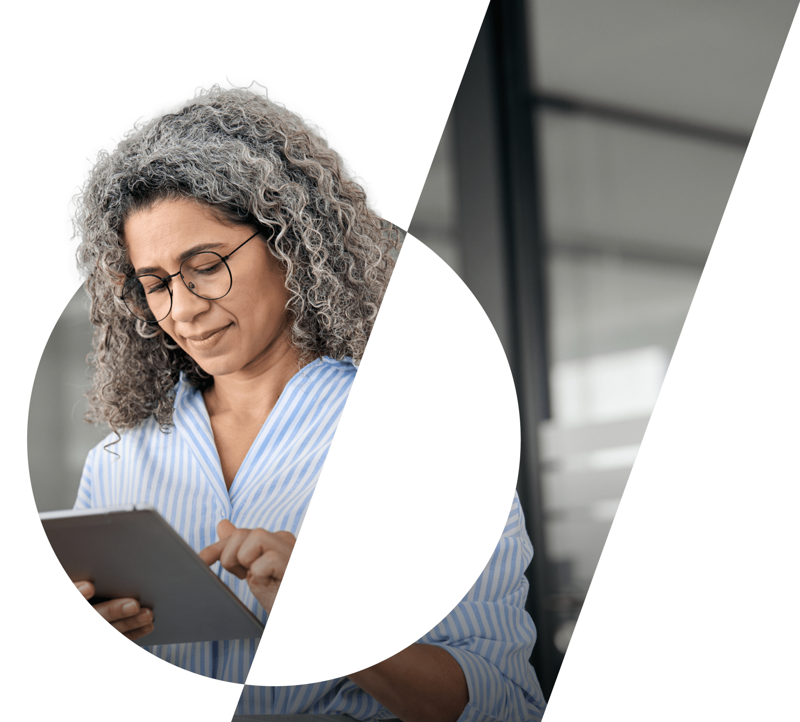 A woman with grey hair looks down at a tablet in an office setting.